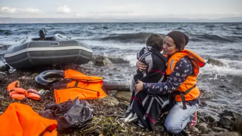 Getty Images A woman holds her child as she arrived with other refugees on the shores of the Greek island of Lesbos