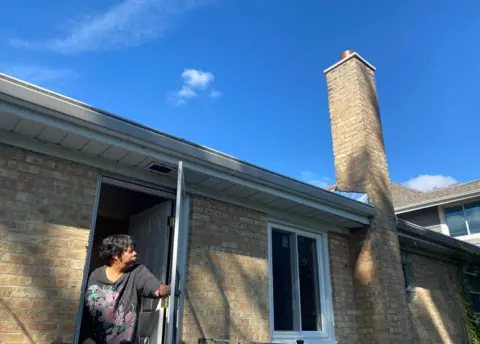 Ramona Burton gazes at her repaired chimney and new windows - work made possible by the first reparations program of its kind