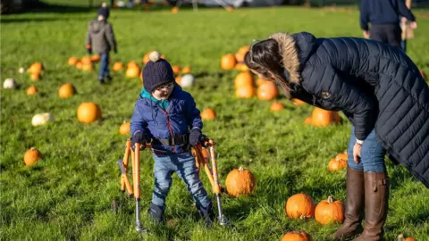 Peter Tranter Photography A boy using a walking frame laughs with a woman in the pumpkin patch