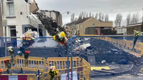 BBC Flowers in a barrier fence outside a devastated terrace home