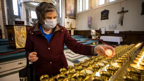 PA Media A woman wearing a face mask lights candles at a church in Northern Ireland