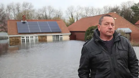 PA Media Kevin Lorryman standing in front of his submerged bungalow