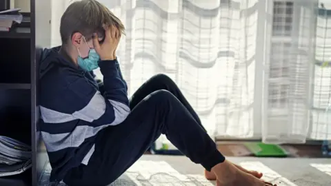 Getty Images A boy with his face in his hands, wearing a mask