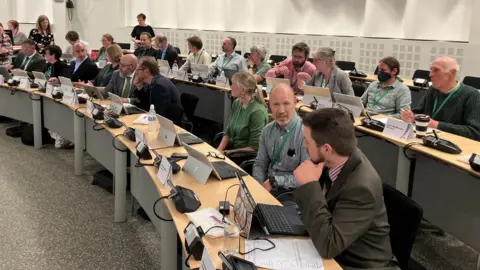 BBC Mid Suffolk District Council meeting with members sitting at their desks