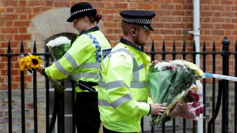 Reuters Police officers carry flowers left at the scene of multiple stabbings in Reading