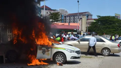AFP People stand next to a police car that has set alight