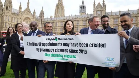 PA Media Several people holding a banner with the hashtag Fight4Pharmacies and the words: "2.5 million GP appointments may have been created by pharmacy closures since 2019 - Stop pharmacy closures"