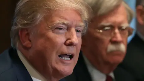 Getty Images U.S. President Donald Trump is flanked by National Security Advisor John Bolton as he speaks about the FBI raid at his lawyer Michael Cohen"s office,