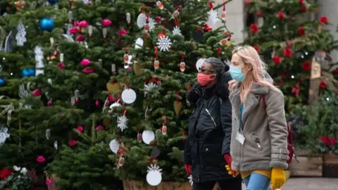 PA Media Two people wearing face masks by Christmas trees