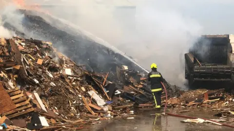 Firefighter blasts water onto woodpile