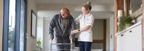 Getty Images Care worker helping patient