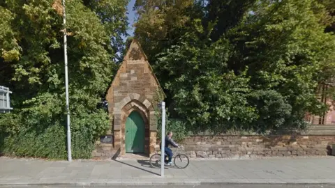 Google Stone arch around a green wooden gate surrounded by trees