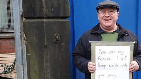 Zia Salik Andrew Graystone holding placard saying: "You are my friends. I will keep watch while you pray."