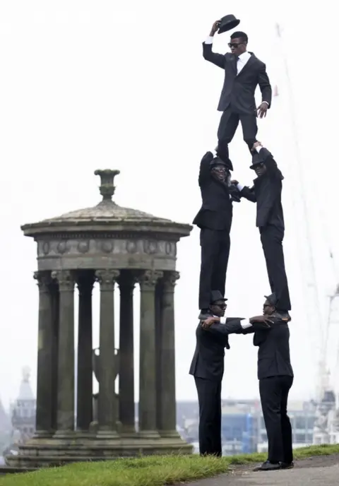PA Media Five acrobats stand in a triangle shape on top of Calton Hill in Edinburgh.