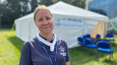 Shaun Whitmore/BBC Nicola Tooke is wearing a scouts t-shirt, standing in front of a white marquee.