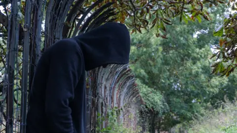 Getty Images person in a hoodie leaning on a fence