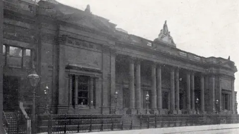 A black and white image of Hull Royal Institution on Albion Street. It is a classical stone building with columns along its entrance and metal railings at the front 