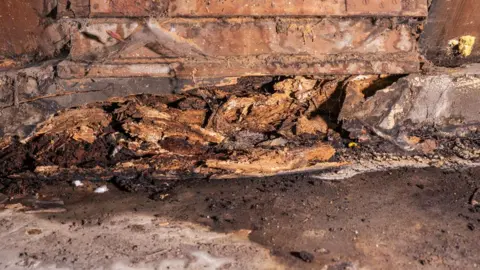 Historic England Archive A close up of sodden roof timbers in the Cathedral of St John the Baptist. The wood has flaked and is dark brown in places where it is wettest. In front is stone, which is dark brown and damp 