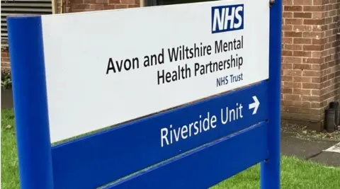 An NHS sign for the now-closed Riverside Unity. It is a largely blue and white sign with some black text