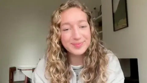 a girl with long, blonde, curly hair smiles at the camera.