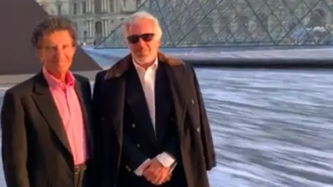 Two middle-aged men stand outside a museum