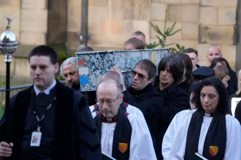 PA Mani's former Stone Roses and Primal Scream bandmates, along with Oasis star Liam Gallagher, carrying his coffin out of the cathedral. The coffin was painted like the cover of the Stone Roses first album.
