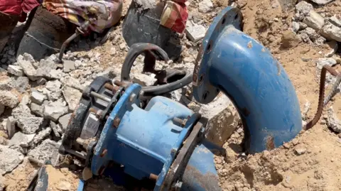 Blue pipes for water are seen amid rubble in Gaza