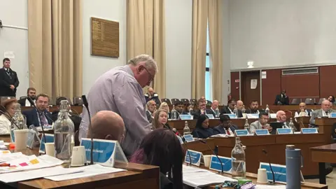 Local Democracy Reporting Service Councillors seated in the Oldham Council chamber, with one councillor standing up to address the meeting
