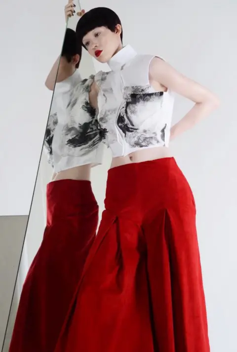 Nadia Pinkney A model wearing a red skirt and white top with black pattern.