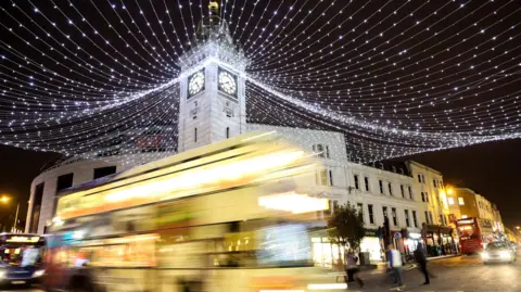 A Brighton and Hove Bus driving past the Clocktower in North Road, blurred, at night, with the streets decorated with strings of white Christmas lights.