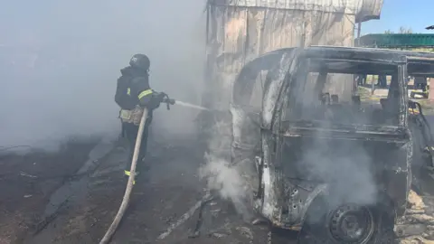 A firefighter trains a hose on a burnt-out vehicle in the Kharkiv region of Ukraine on 7 May following Russian drone strike