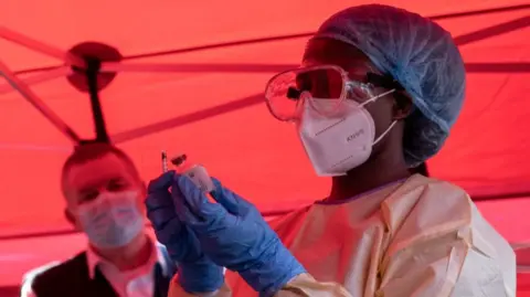A nurse wearing protective medical clothing prepares a syringe during an Ebola trial vaccination campaign in Uganda