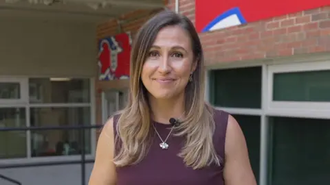 Sarah Dawkins, BBC Sport reporter, smiling down the lens wearing a maroon top and silver necklace