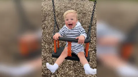 Kirsty Pedelty AJ, a blonde toddler with Down's Syndrome, laughs while on a swing