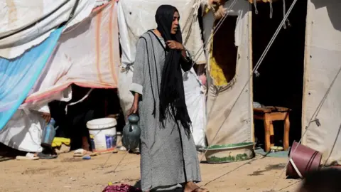 A displaced Sudanese woman walks next her tent at "Abdallah Nagi" shelter camp, which houses people mostly displaced from the capital Khartoum, in Port Sudan.
