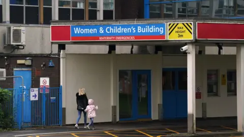 PA Media The entrance to the Women and Children's Building at the Countess of Chester Hospital. A blonde woman in a black coat walks under a sign for the building hand-in-hand with a young girl in a pink coat. 