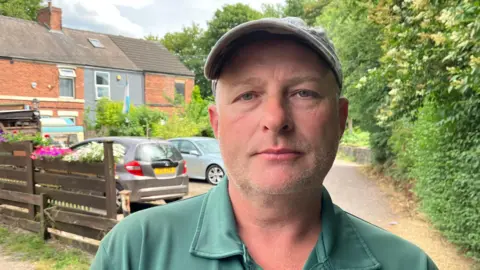 A man in a green polo-neck top stood in a garden