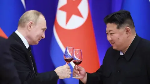 Getty Images Vladimir Putin e Kim Jong desmoronam um ao outro com copos de vinho tinto, em frente às bandeiras russas e norte -coreanas