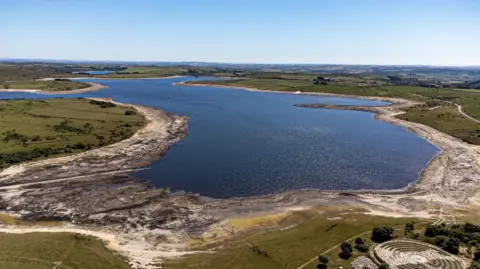 This is an aerial photo taken from a drone of Colliford Lake in August 2022, where water levels had severely dropped exposing rocks. A circular stone maze can be seen to the bottom right of the lake.