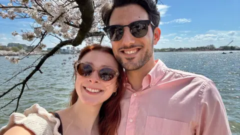 Yaron Lischinsky and Sarah Milgrim, both wearing sunglasses and smiling, with water in the background