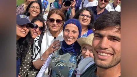 Women from the Carolle & Iman Tennis with defending men's champion Carlos Alcaraz in a selfie at Wimbledon.