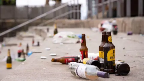 Getty Images A number of glass bottles can be seen scattered on a set of steps. There is wine bottle in the foreground alongside a few cider bottles. Just behind them, a smashed Budweiser beer bottle can be seen.
