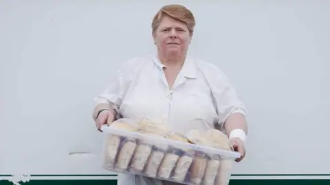 Mark Griffiths A woman dressed in white overalls holds a large plastic container holding bread rolls for her burger van used by steelworkers