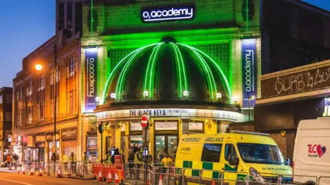 Getty Images An exterior, night-time shot of the O2 Academy Brixton, with a sign showing the Black Keys were playing, the dome on the facade lit up in green neon and an ambulance parked outside