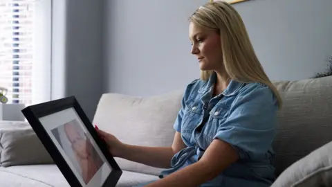 Alex Grace Photography A woman on a sofa looking at a picture of her baby