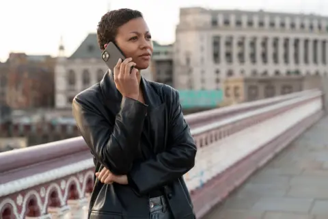 BBC/Bad Wolf Productions/HBO/Nick Strasburg A woman is dressed with a black leather coat on a bridge, with a phone to her ear