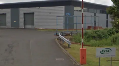 Google A empty tarmac road leading to an empty car park of a silver metal-clad industrial unit 