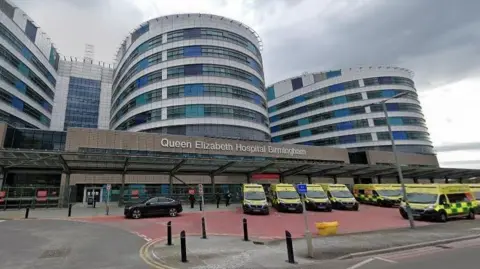 The outside of Queen Elizabeth Hospital in Birmingham with a fleet of ambulances lined up in front of it. 