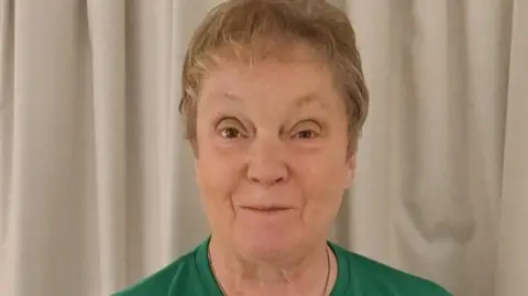Helen Fisher Helen Fisher, wearing a green top, stands in front of beige curtains.