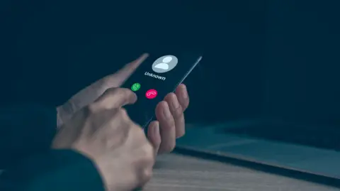 The image shows someone holding a mobile phone in a dark room, with the word "Unknown" on the screen with the red and green button to accept or decline.